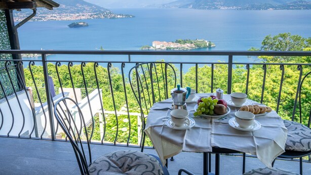 Ein Balkon mit Frühstückstisch, Blick auf einen See und Berge.