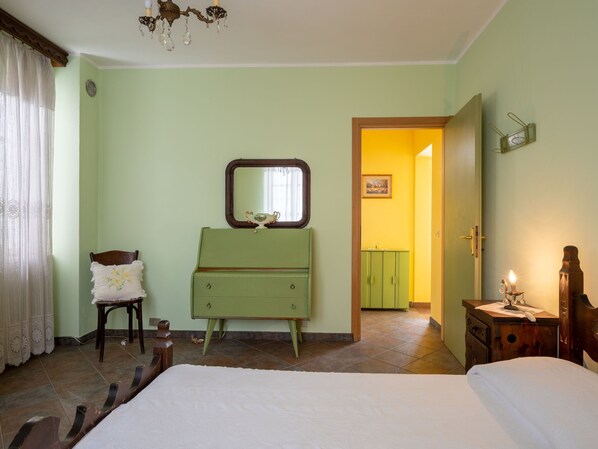 A bedroom with a bed, a green dresser, a chair, a mirror, and a door leading to another room.