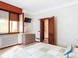 A room with a bed, a dresser, a television mounted on the wall, and a door leading to another room.