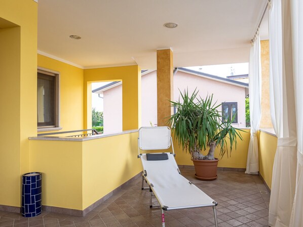 A balcony with yellow walls, a white reclining chair, a potted plant, and a blue trash bin. - Bonatti by Interhome (Sirmione)