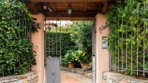 A stone-walled entrance with a metal gate, surrounded by lush greenery and potted plants. - La Casetta by Interhome (Diano Marina)