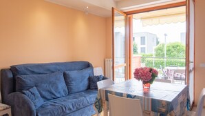 Un salon avec un canapé bleu, une table à manger avec des chaises et un balcon offrant une vue sur les bâtiments et la verdure.