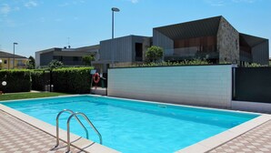 Une piscine dotée d’une terrasse carrelée, d’une bouée de sauvetage et d’un bâtiment moderne à la façade en pierre.