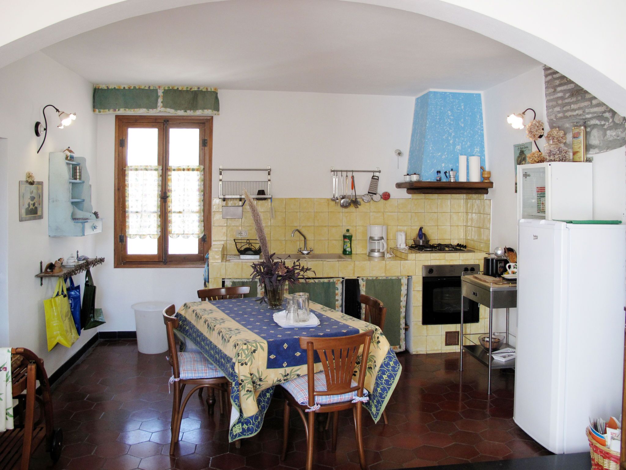 A kitchen with a dining table, chairs, a refrigerator, and a window with curtains.