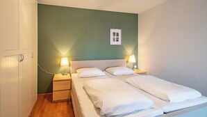 A twin bed with white linens in a room with green walls, two bedside tables with lamps, and a framed picture on the wall. - Apartment in Bergen near Sandy Beach (Callantsoog)