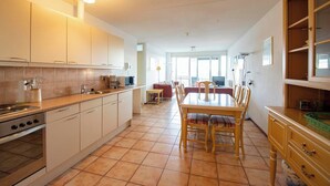 A spacious kitchen with white cabinets, a dining table with chairs, and a large window providing natural light. - Apartment in Bergen near Sandy Beach (Callantsoog)