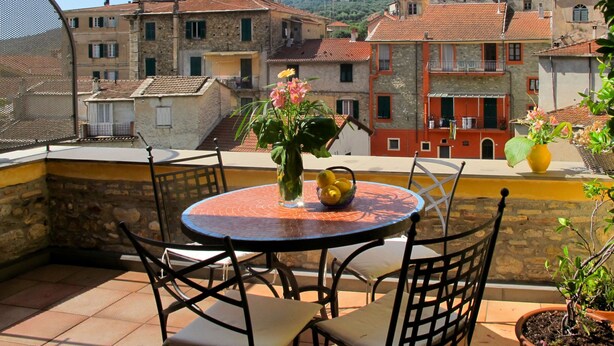 Eine Terrasse mit rundem Tisch und Stühlen, einer Blumenvase, einem Zitronenkörbchen und einem Blumentopf.