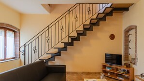 A living room with a black staircase, a sofa, a TV, and a bookshelf. - Vince (DOX200) by Interhome (Dorio)