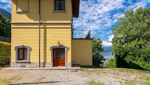 A two-story yellow building with a wooden door and windows, a balcony, and a view of a lake with boats. - Vince (DOX200) by Interhome (Dorio)