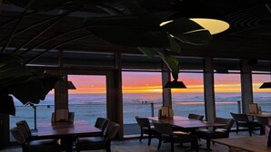 Een restaurant met grote ramen en uitzicht op de oceaan bij zonsondergang.