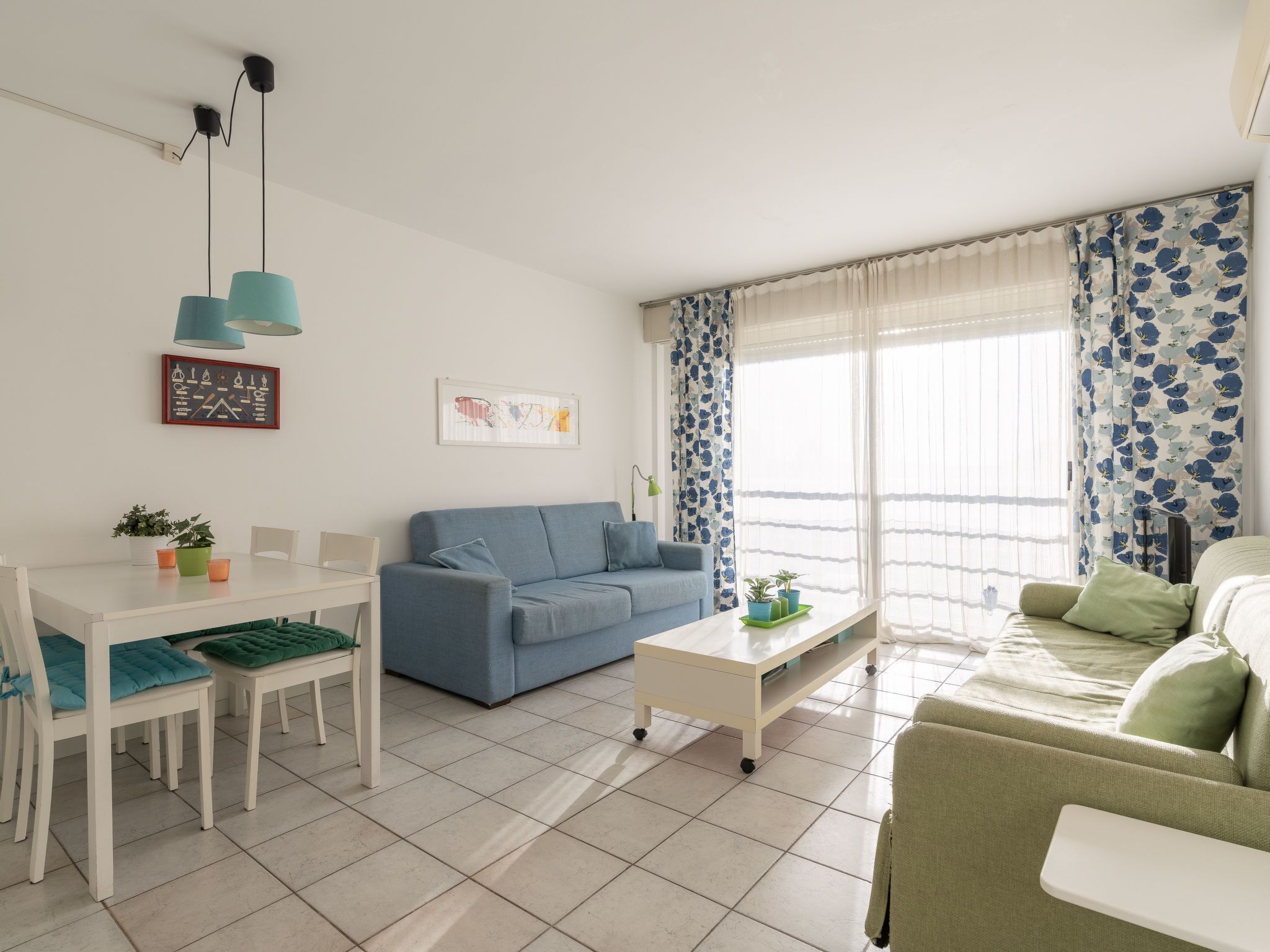 Ein modernes Wohnzimmer mit einem blauen Sofa, einem grünen Sofa, einem weißen Esstisch mit Stühlen und einem Couchtisch.