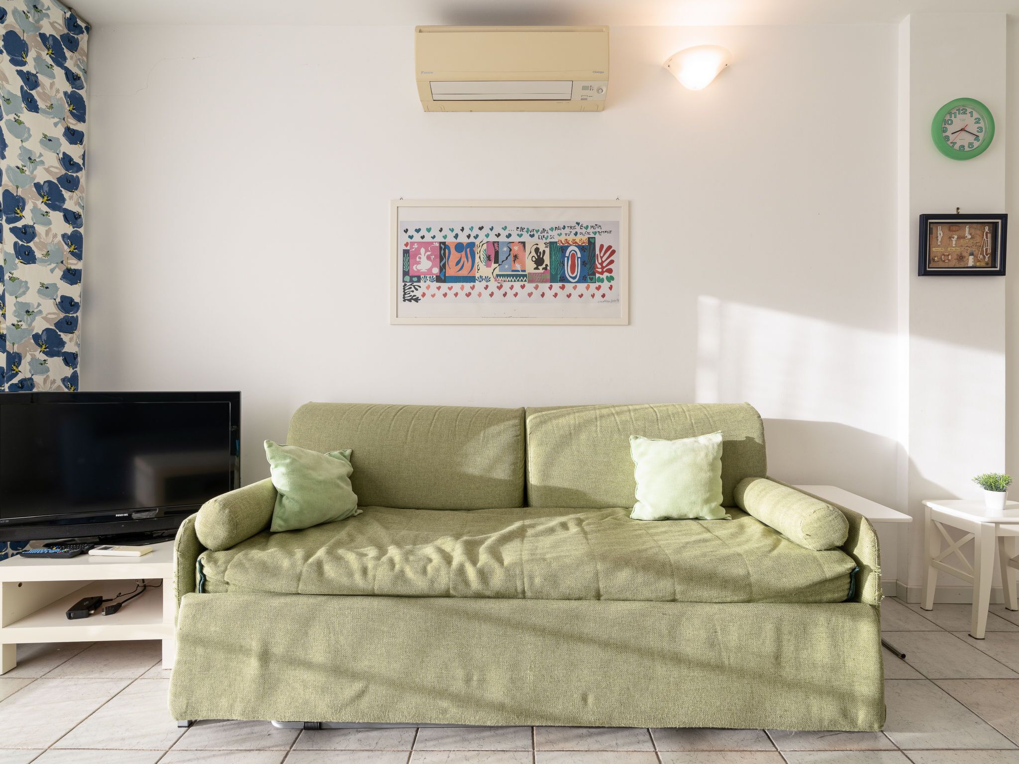 Ein Wohnzimmer mit einem grünen Sofa, einem Flachbildfernseher und einem gerahmten Kunstwerk an der Wand.