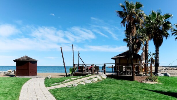 A beachside property with a paved walkway leading to a wooden deck area, a small hut, and a palm tree. - Apartment Sara by Interhome (Santo Stefano al Mare)