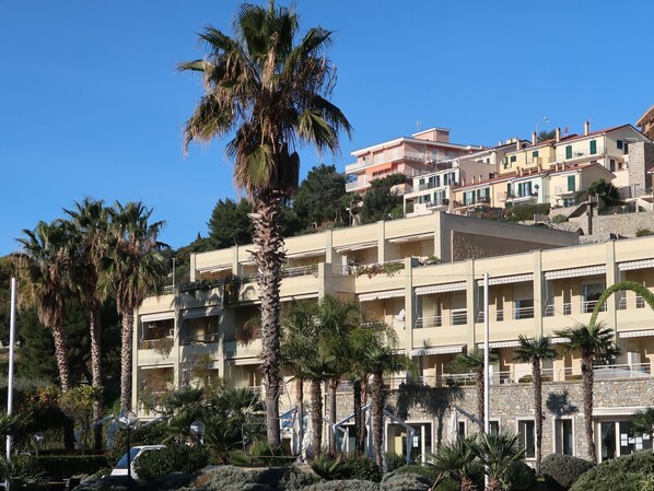 A multi-story building with balconies, surrounded by palm trees and greenery.