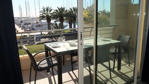 A balcony with a glass door, a table set for two, and a view of boats and palm trees.