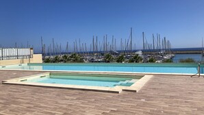 A swimming pool with a wooden deck, surrounded by a marina with numerous boats.