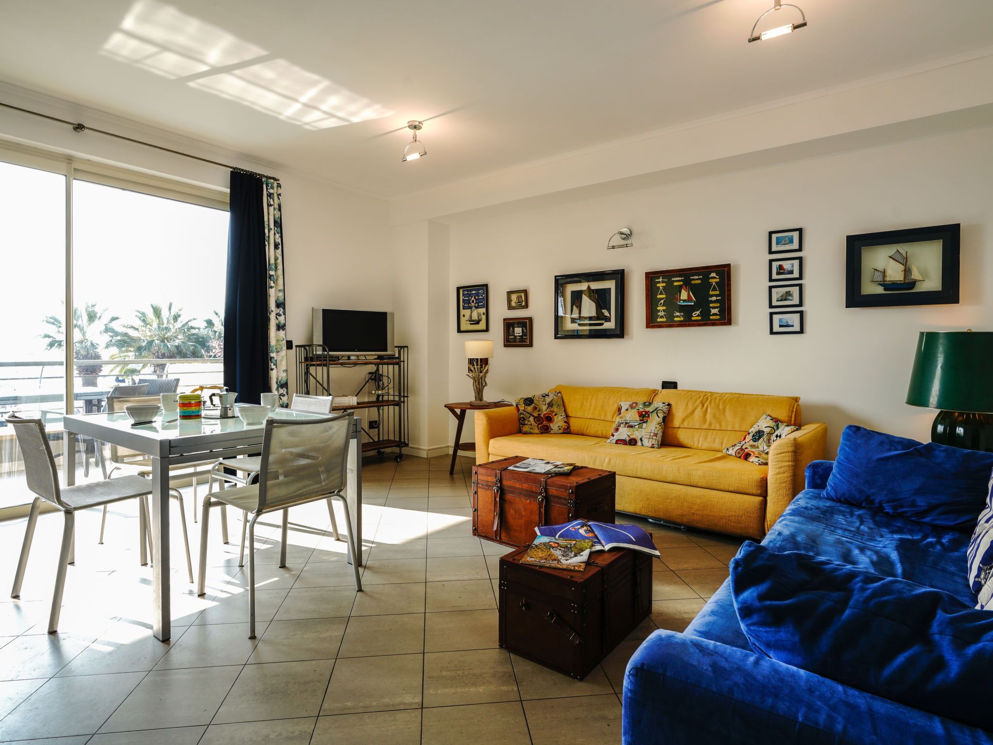 Una sala de estar con un sofá amarillo, un sofá azul y una zona de comedor con una mesa de vidrio y sillas.