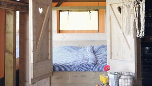 Une cabane en bois chaleureuse, avec un lit, une fenêtre et une table préparée pour le petit-déjeuner, comprenant des œufs, une fraise et une carafe de jus d’orange.