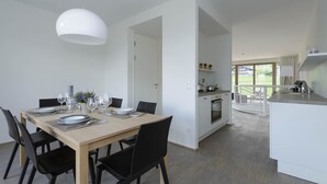 A modern dining area with a wooden table set for four, black chairs, and a white pendant light.