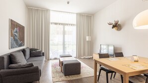 A modern living room with a sofa, a dining table, and a large window with curtains.