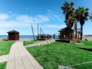 Une propriété située en bord de mer, avec un chemin pavé menant à une terrasse en bois, un petit abri et un palmier.
