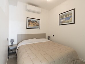 Une chambre à coucher avec un lit, une table de chevet, une lampe et deux tableaux encadrés accrochés au mur.
