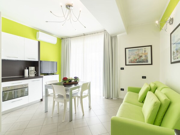 Une cuisine moderne avec des meubles blancs, une table à manger avec des chaises, un canapé vert et un lustre.