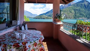 A balcony with a bed, a table with two cups, and a view of a lake and mountains. - Terrazzo fiorito by Interhome (Musso)