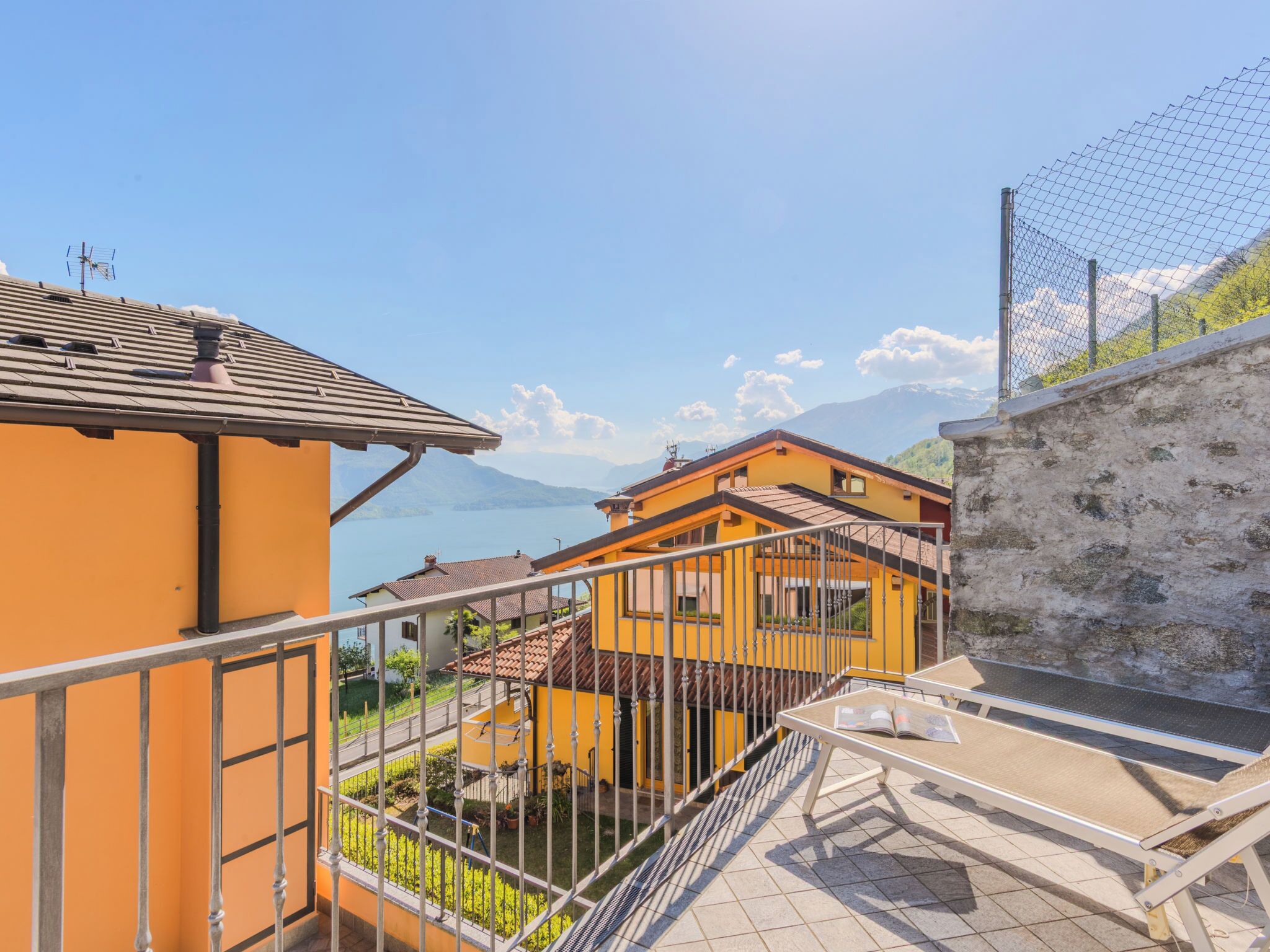 Un balcon donnant sur un lac et des montagnes, un immeuble jaune et une rambarde en métal.