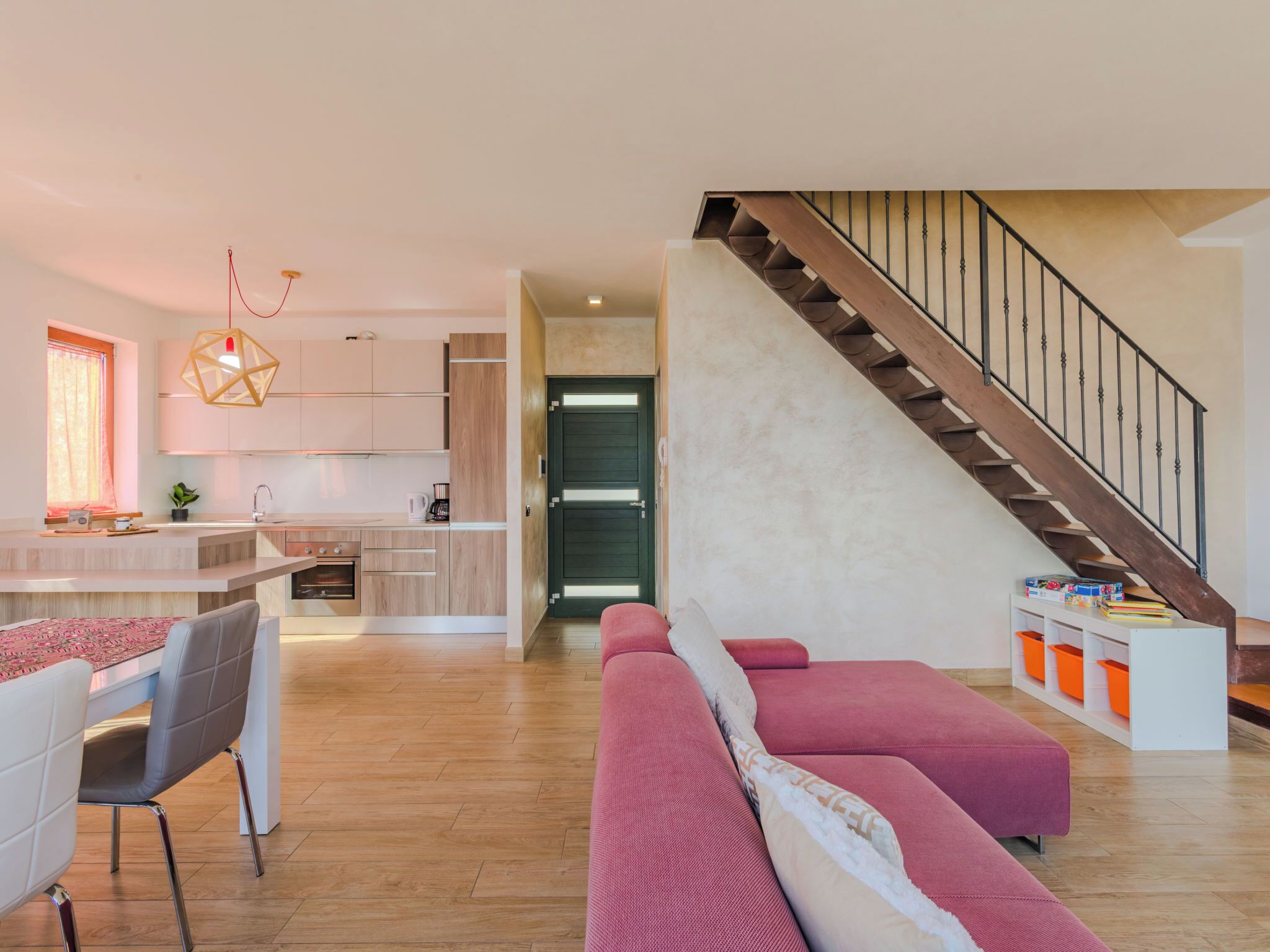 Une cuisine moderne avec un îlot central, un coin repas avec une table et des chaises, un escalier et un espace de vie avec un canapé.