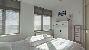 A bedroom with two beds, a white wardrobe, a radiator, and a window with blinds. - Wijde Blick 205 apartment with balcony (Callantsoog)