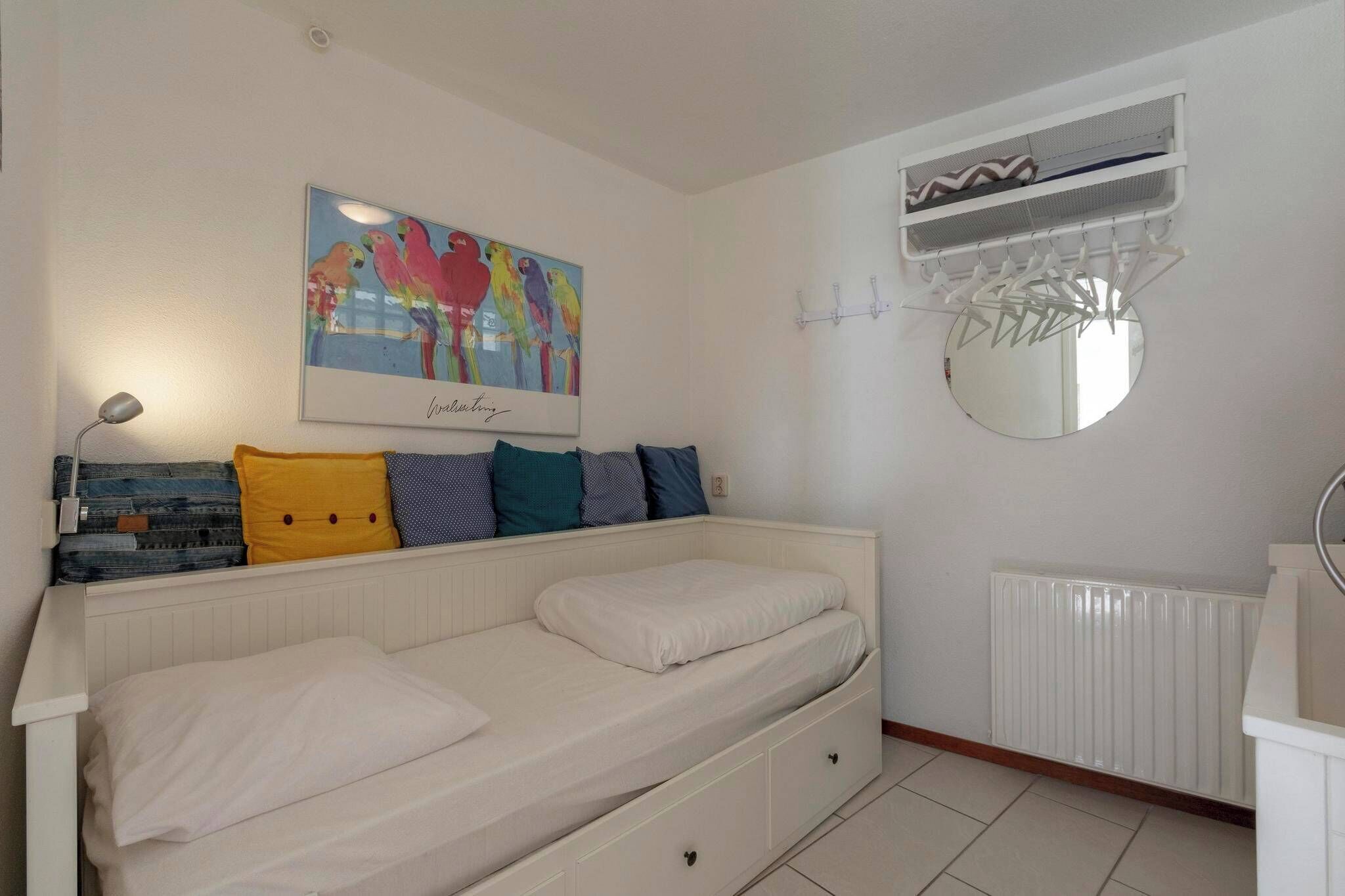 Un dormitorio con cama, unidad de aire acondicionado montada en la pared, radiador y un cuadro colorido sobre la cama.
