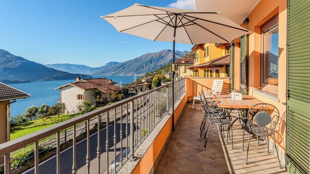 Varanda com mesa e cadeiras, vista para um lago e montanhas.