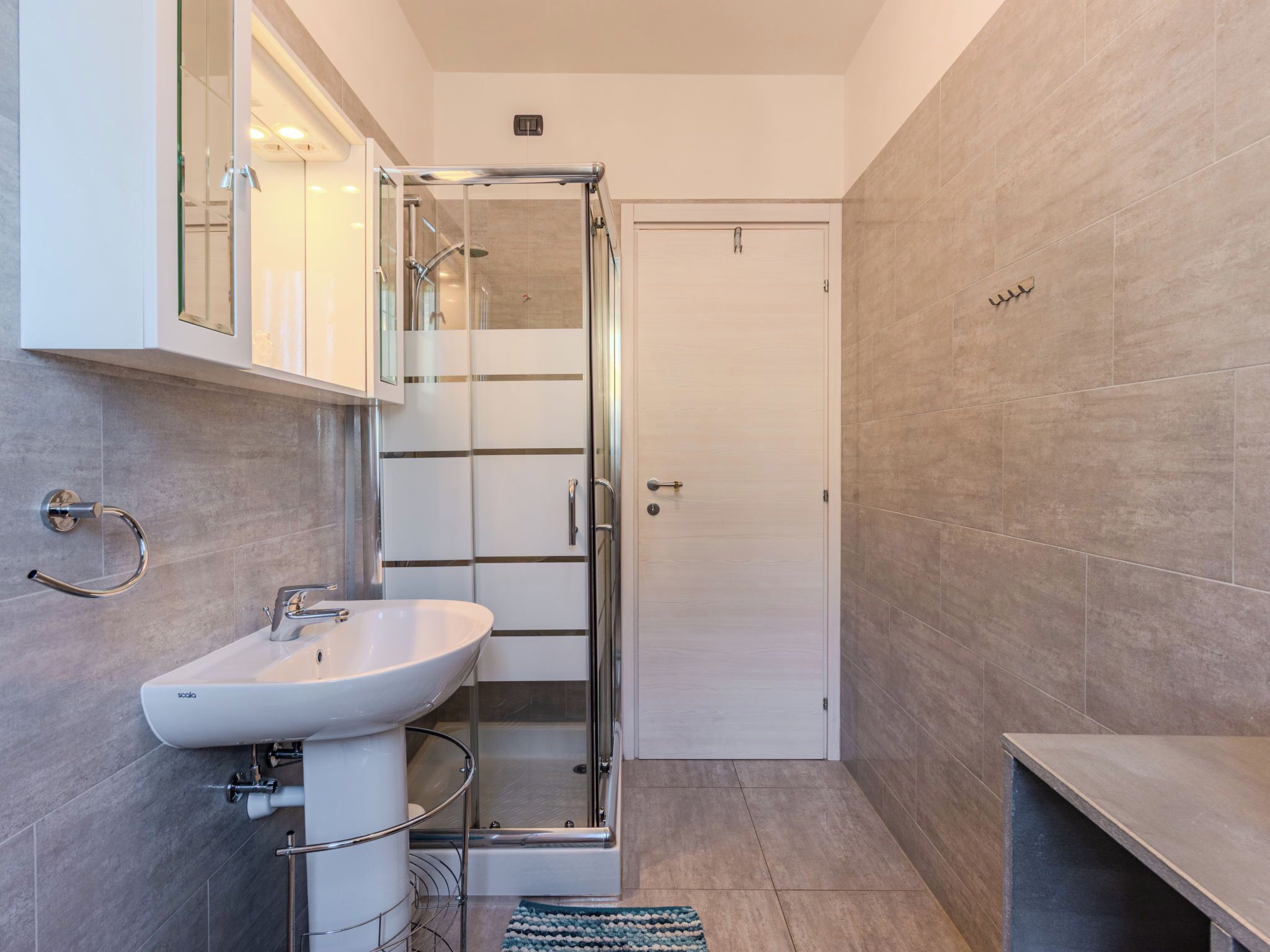 A modern bathroom with a glass-enclosed shower, a white sink, and a tiled floor.
