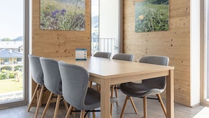 Una sala de reuniones moderna con una mesa de madera y sillas grises, ventanas amplias con vistas a edificios y dos cuadros enmarcados con motivos botánicos en las paredes.
