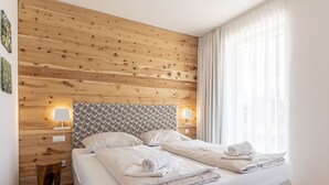 Una cama bien hecha con sábanas y toallas blancas, un cabecero de madera con un diseño estampado, dos lámparas de noche y una ventana con cortinas de encaje.