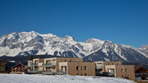 Un hotel moderno con varios pisos, balcones y vistas a montañas nevadas.