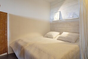 A bedroom with a bed, white bedding, a headboard with a picture, and a wicker chair.