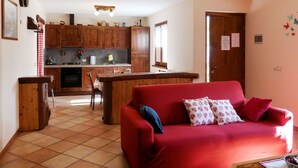 Ein gemütliches Wohnzimmer mit einem roten Sofa, einem Holztisch und einer Küche im Hintergrund.