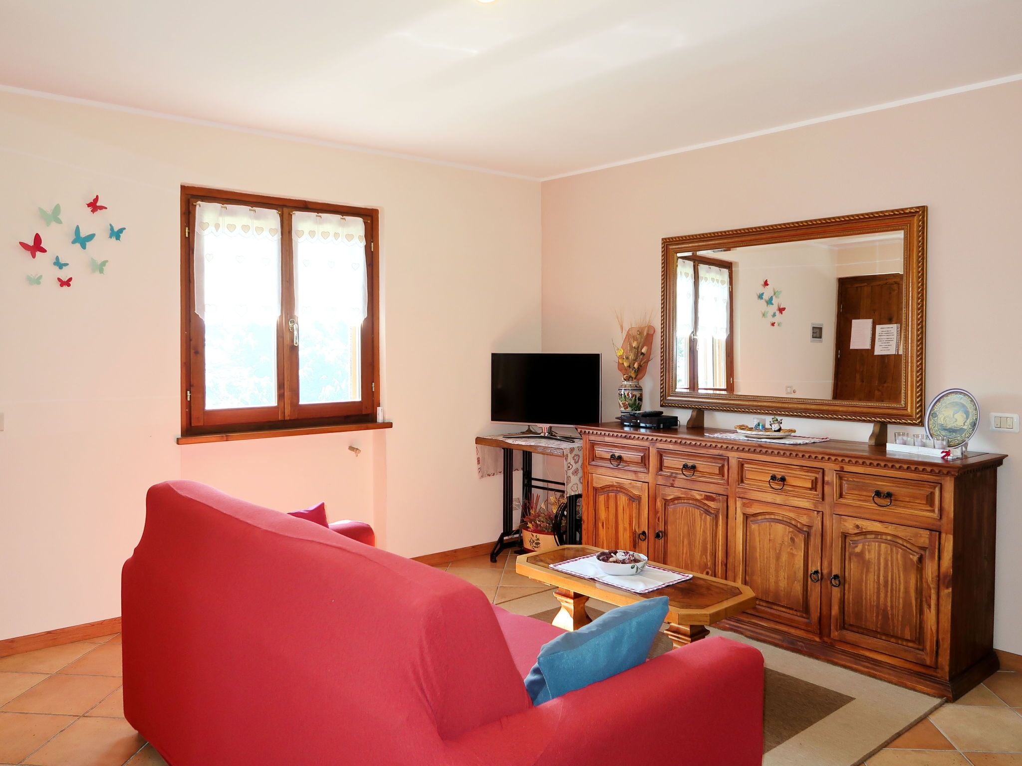 A living room with a red sofa, a wooden cabinet, a television, and a window with curtains.