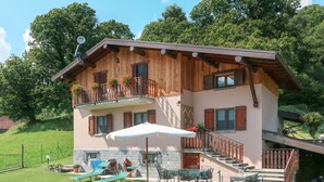 Ein zweistöckiges Holzhaus mit Balkon, Sitzgelegenheit im Freien und einer Steinmauer.