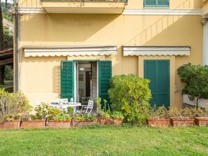 A yellow building with green shutters, a small patio with a table and chairs, and potted plants. - Apartment Botti by Interhome (Ventimiglia)