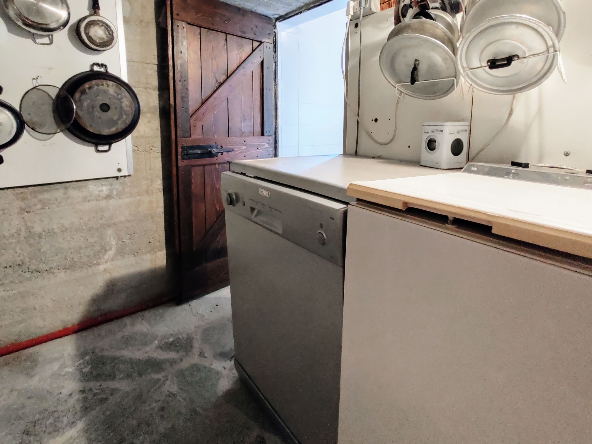 A compact kitchen with a dishwasher, a wooden door, and a wall-mounted stove.