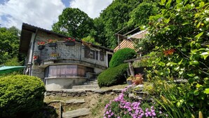 A stone building with a balcony, surrounded by lush greenery and flowering plants. - Baita dei Nonni by Interhome (Gravedona)
