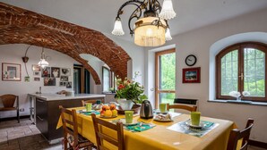 A dining area with a yellow tablecloth, wooden chairs, a chandelier, and a brick archway. - Vacation home Carla by Interhome (Cortazzone)