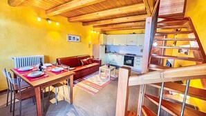 A cozy room with a wooden ceiling, a dining table set with plates and a bottle, a sofa, and a kitchen in the background. - Le Baite di Bodone by Interhome (Gravedona)