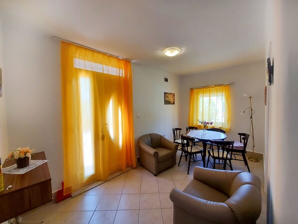 A dining area with a round table and chairs, a sofa, and a curtain with a window.