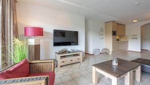 Sala de estar con televisor, sofá y mesa de centro. Cuenta con una zona de cocina con armarios y microondas.