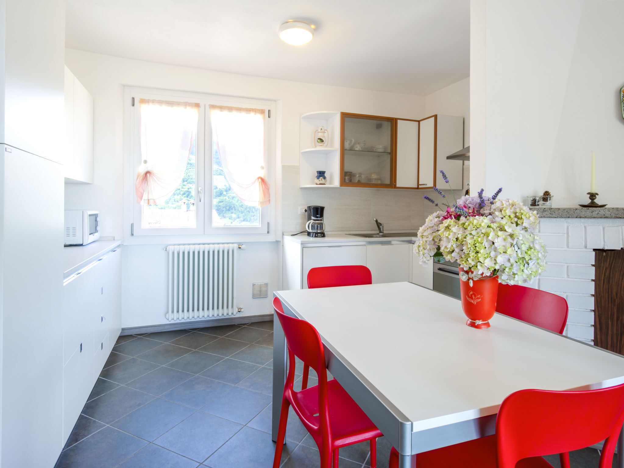 Een moderne keuken met witte kastjes, een rode eettafel en een bloevas.