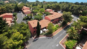 An aerial view of a coastal residential area with terracotta-roofed buildings, a curved road, and a clear view of the sea. - Les Chênes Verts by Interhome (Saint-Raphaël)